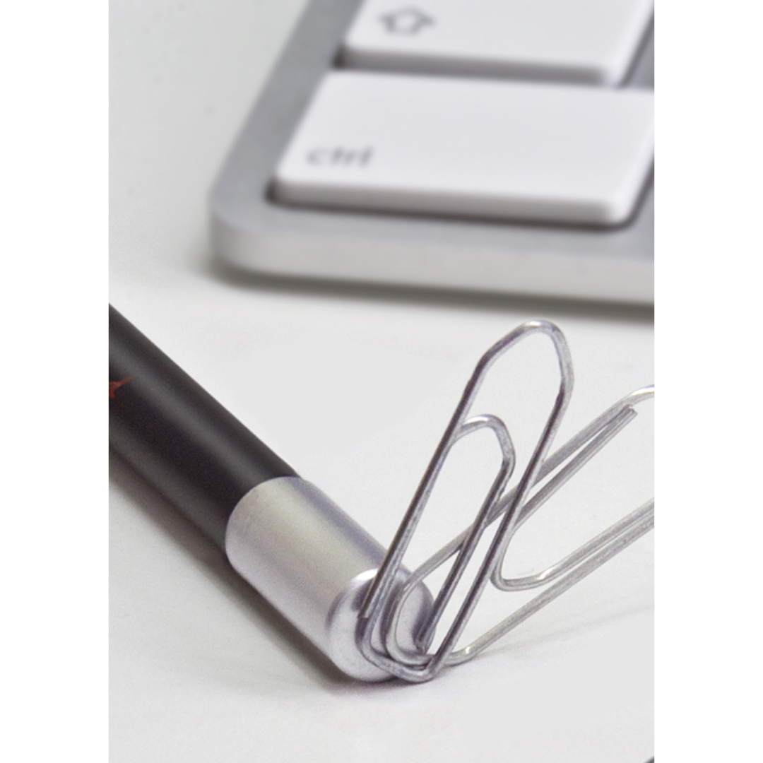 Detailansicht des oberen Teils eines Magnetbleistifts mit silberner magnetischer Kappe und zwei daran haftenden Büroklammern vor der unteren Ecke einer PC-Tastatur