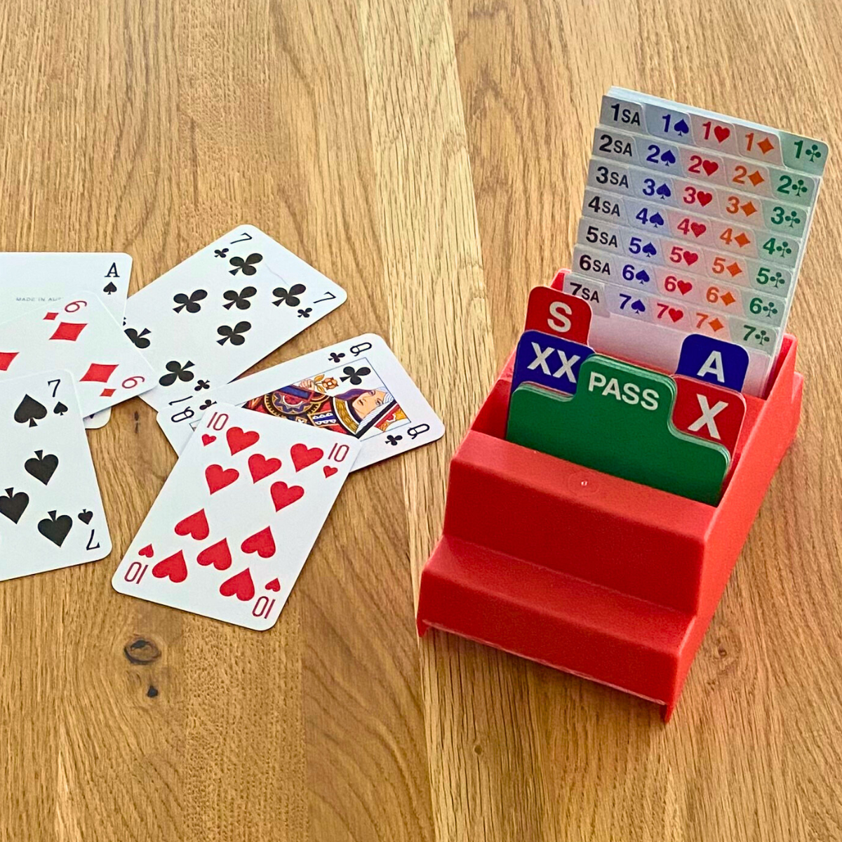 Bidding Box mit eingesteckten Bietkarten sowie einige Spielkarten auf Holztisch