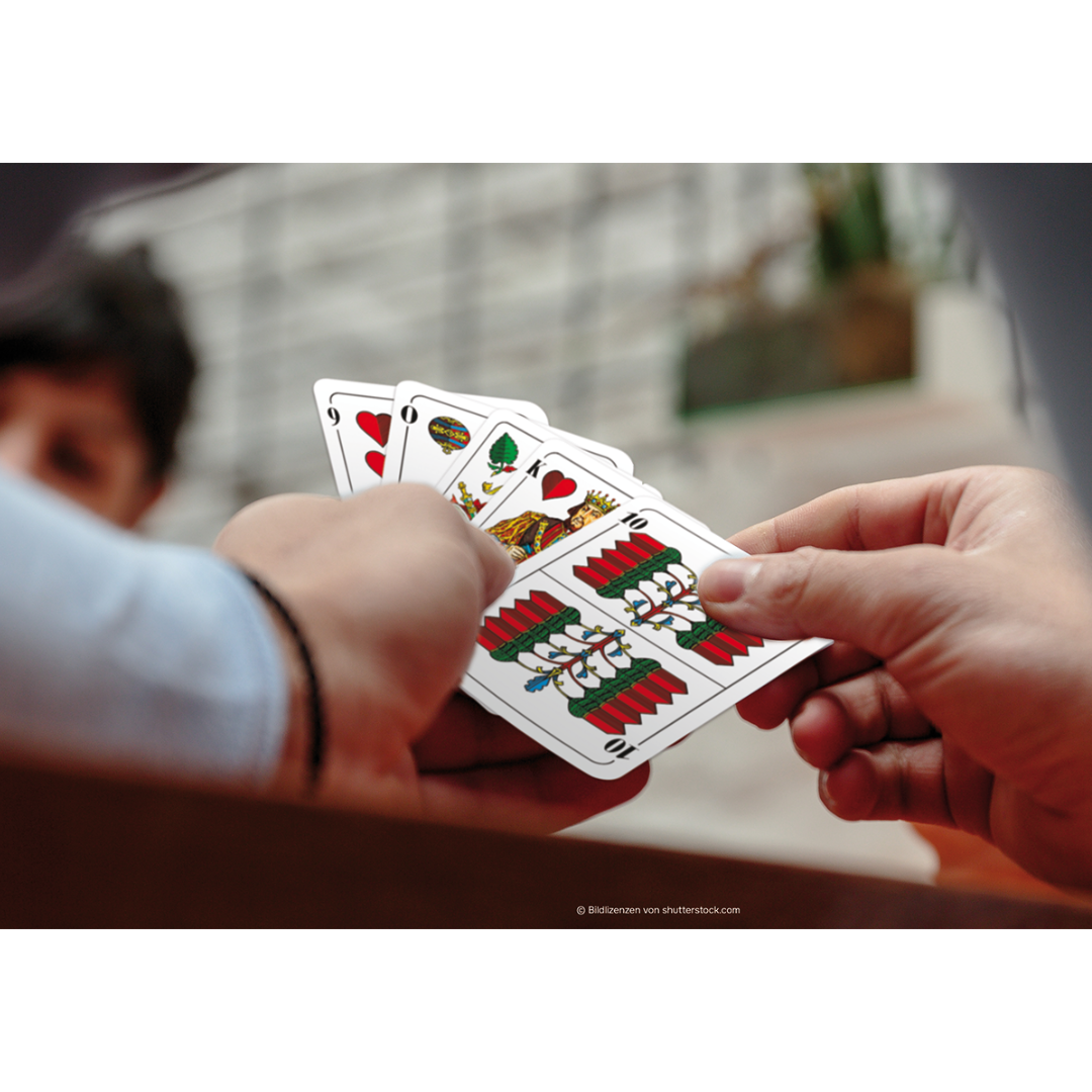 Eine Hand hält einen Kartenfächer mit den ASS Doppelkopf Spielkarten mit deutschem Bild.