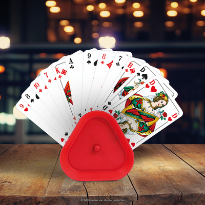 Roter Spielkartenhalter aus Kunststoff mit Spielkarten präsentiert im Scheinwerferlicht auf einem Holztisch.