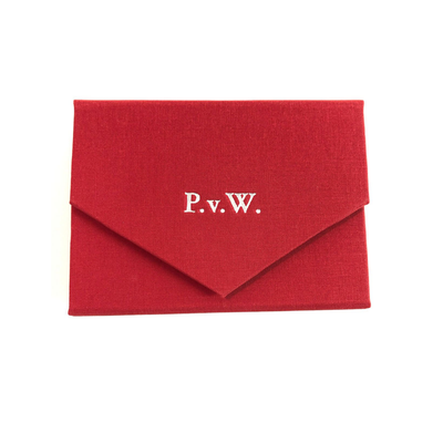 Ein geschlossenes Spielkarten-Etui bezogen mit rotem Stoff mit einem  silber geprägten Monogramm P.v.W. auf der Verschlusslasche.